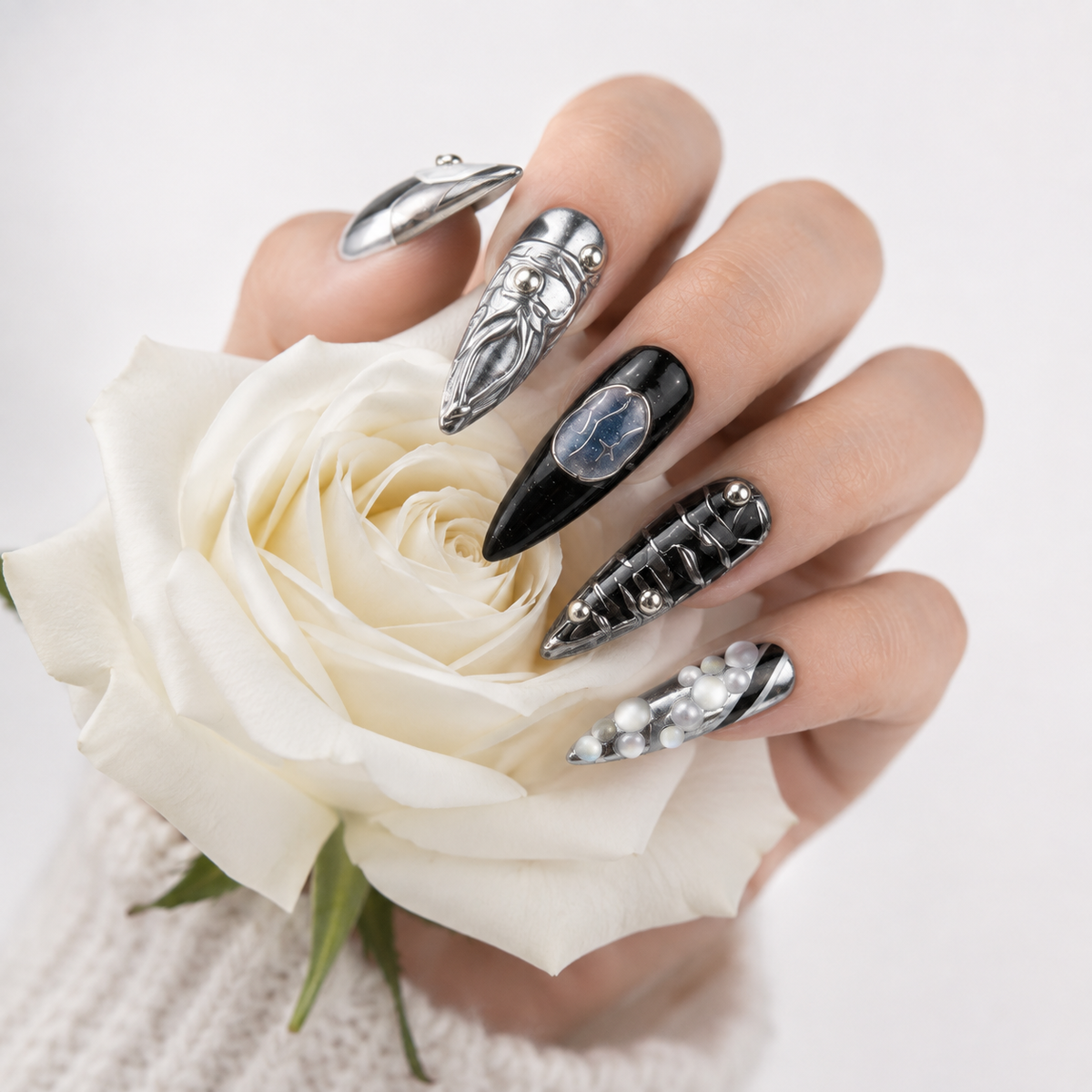 Black chrome press on nails with blue gemstone details holding a white rose