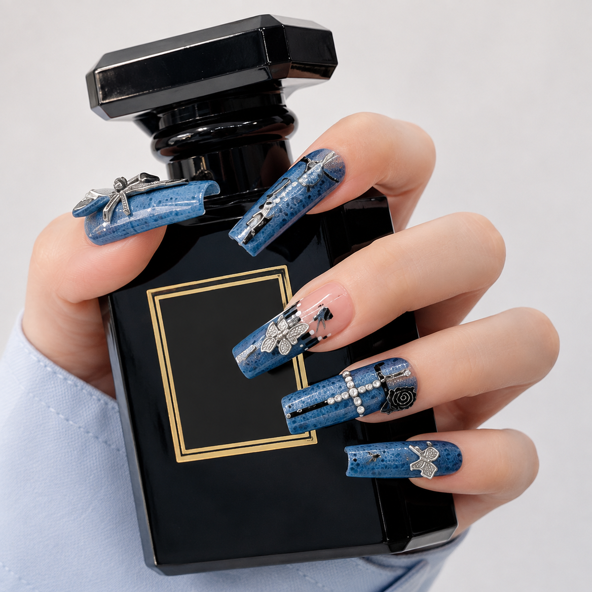 Blue Denim Press On Nails with Silver Charms Holding a Black Perfume Bottle