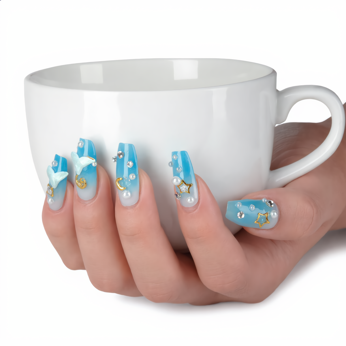 Blue ombre press on nails with celestial charms styled with a white coffee cup