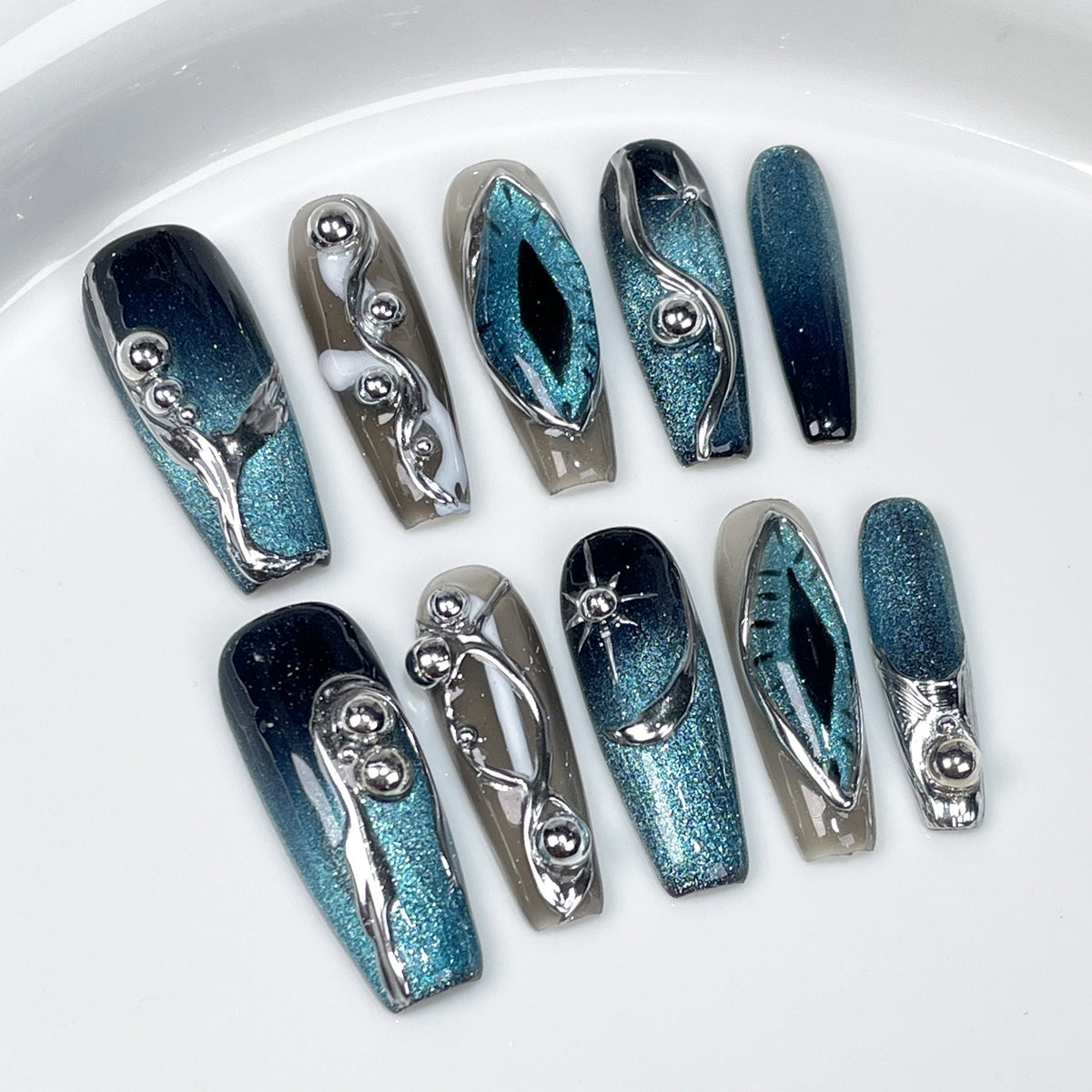 Blue teal cat eye chrome 3D press on nails with metallic silver accents on hand, luxury handmade reusable fake nails, white background.