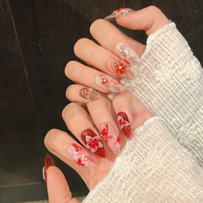 Both hands wearing luxury red floral almond press on nails with handcrafted 3D flowers, glossy finish and reusable salon-quality fake nails.