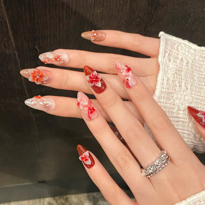 Both hands wearing luxury red floral almond press on nails with handcrafted 3D flowers, glossy finish and reusable salon-quality fake nails.