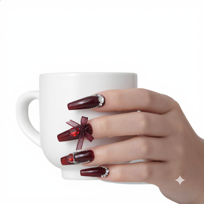Burgundy rhinestone press on nails with 3D bow holding a white coffee cup