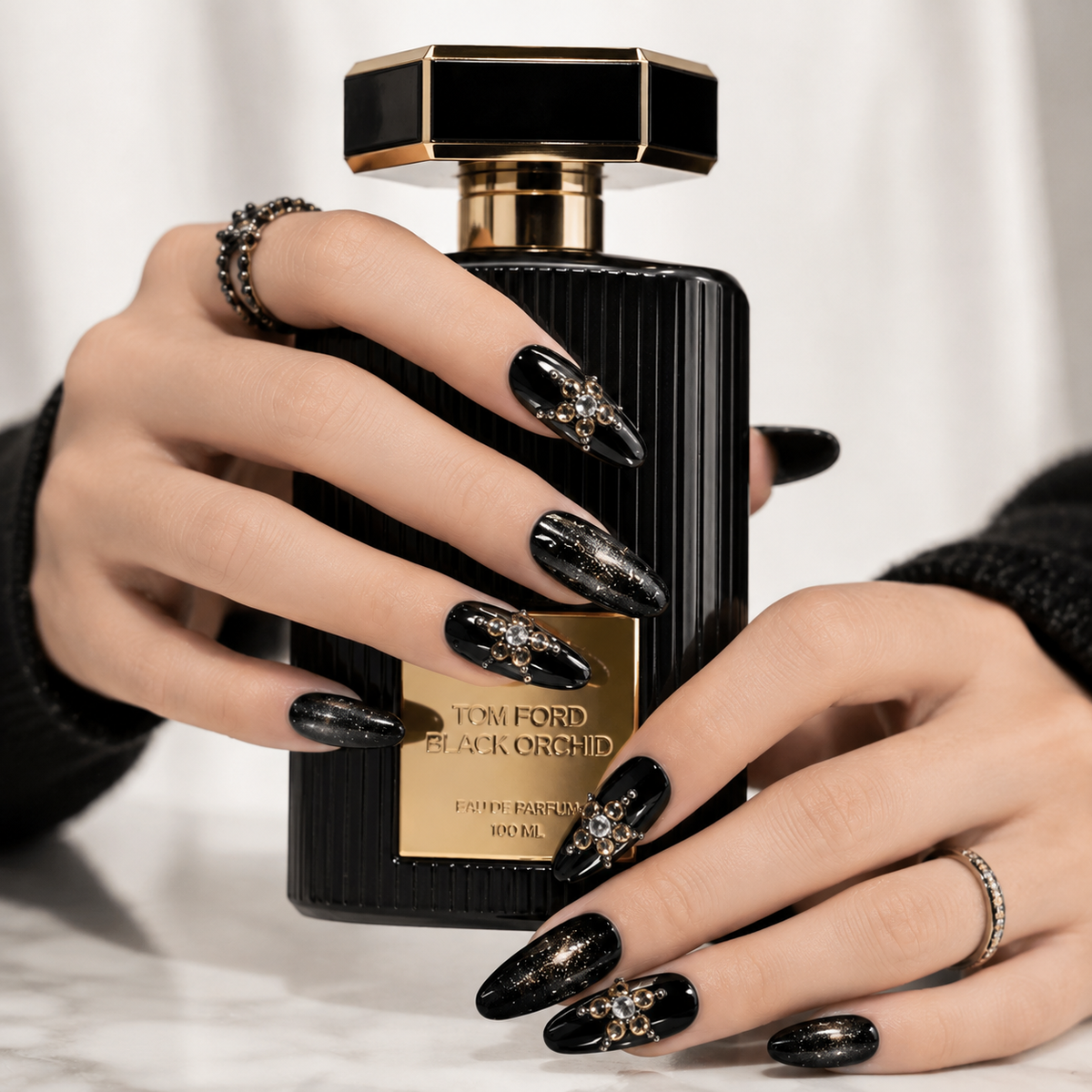 Elegant black glitter press on nails holding a luxury perfume bottle, handcrafted crystal almond fake nails with premium reusable finish.