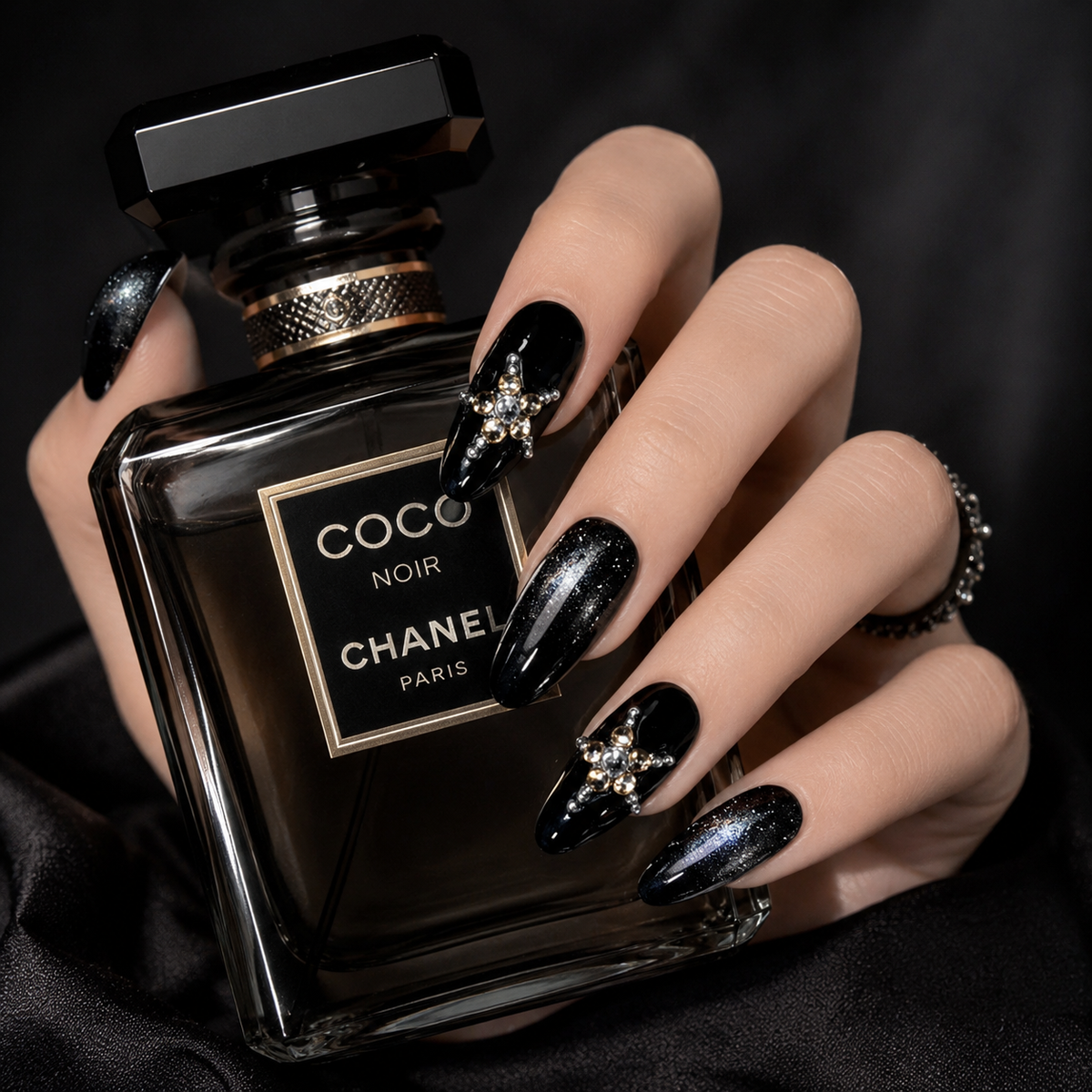 Luxury black crystal press on nails holding a premium black perfume bottle, handmade glitter almond fake nails with elegant rhinestone details.