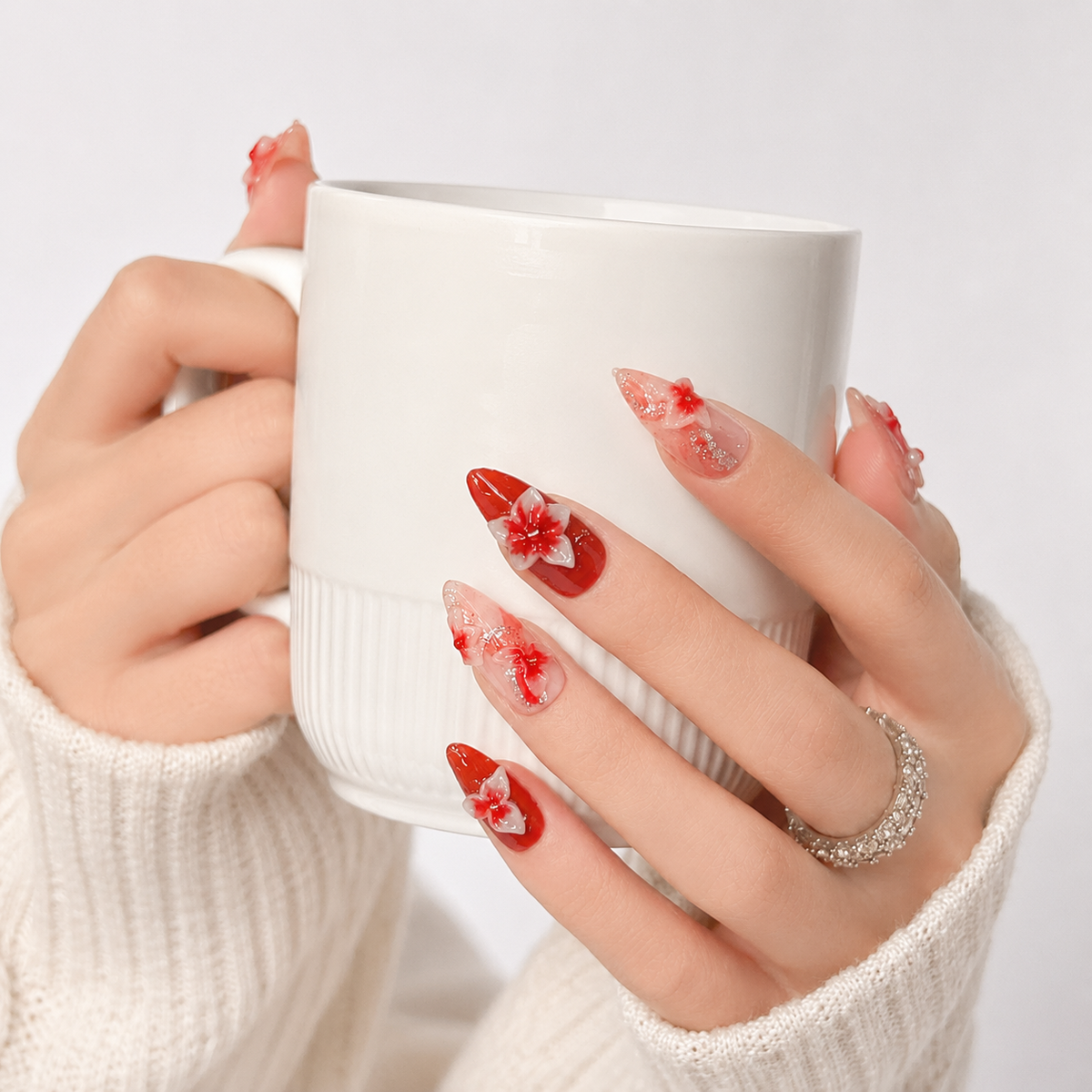 Luxury red floral 3D almond press on nails holding a white coffee cup, handcrafted reusable fake nails with elegant flower details.