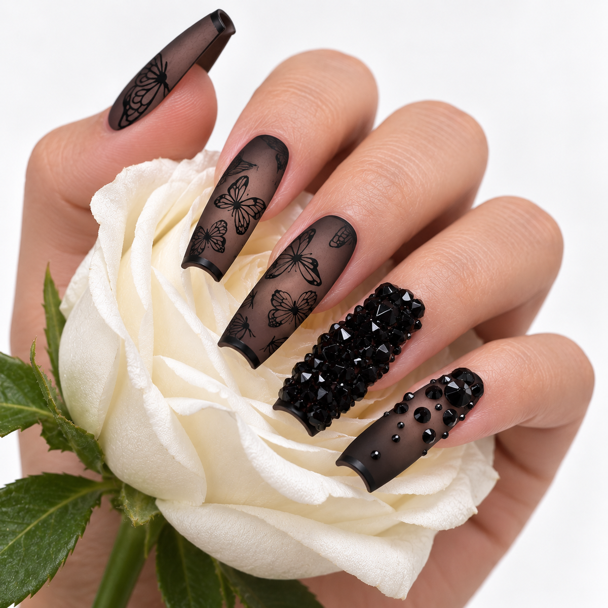 Black butterfly press-on nails with rhinestone details styled with a white rose