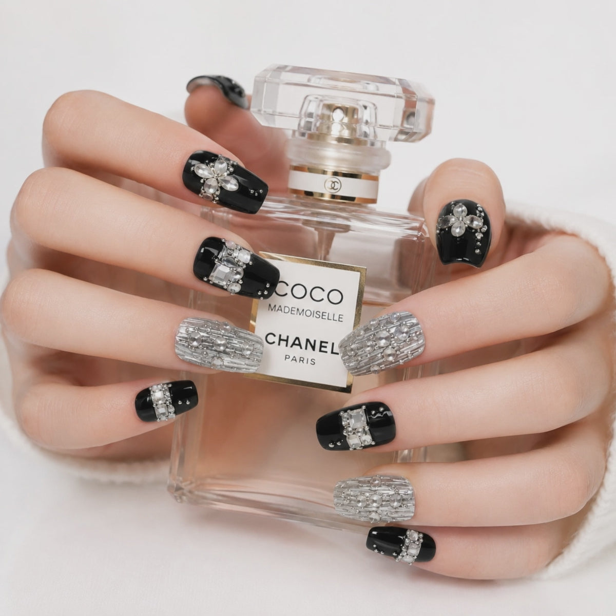 Luxury black and silver crystal press on nails holding a perfume bottle